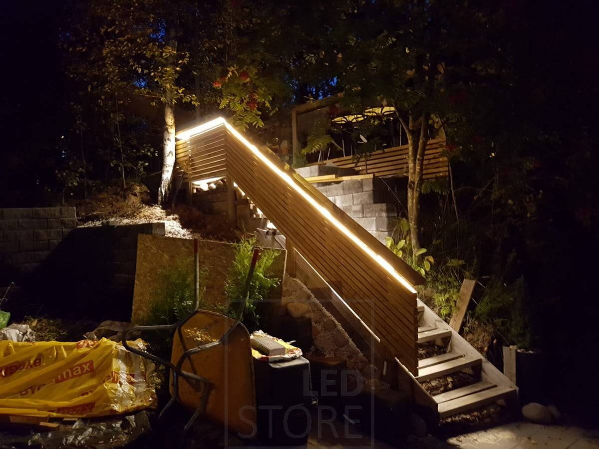 Bande LED montée sur la rampe d'un escalier extérieur pour éclairer indirectement les marches.